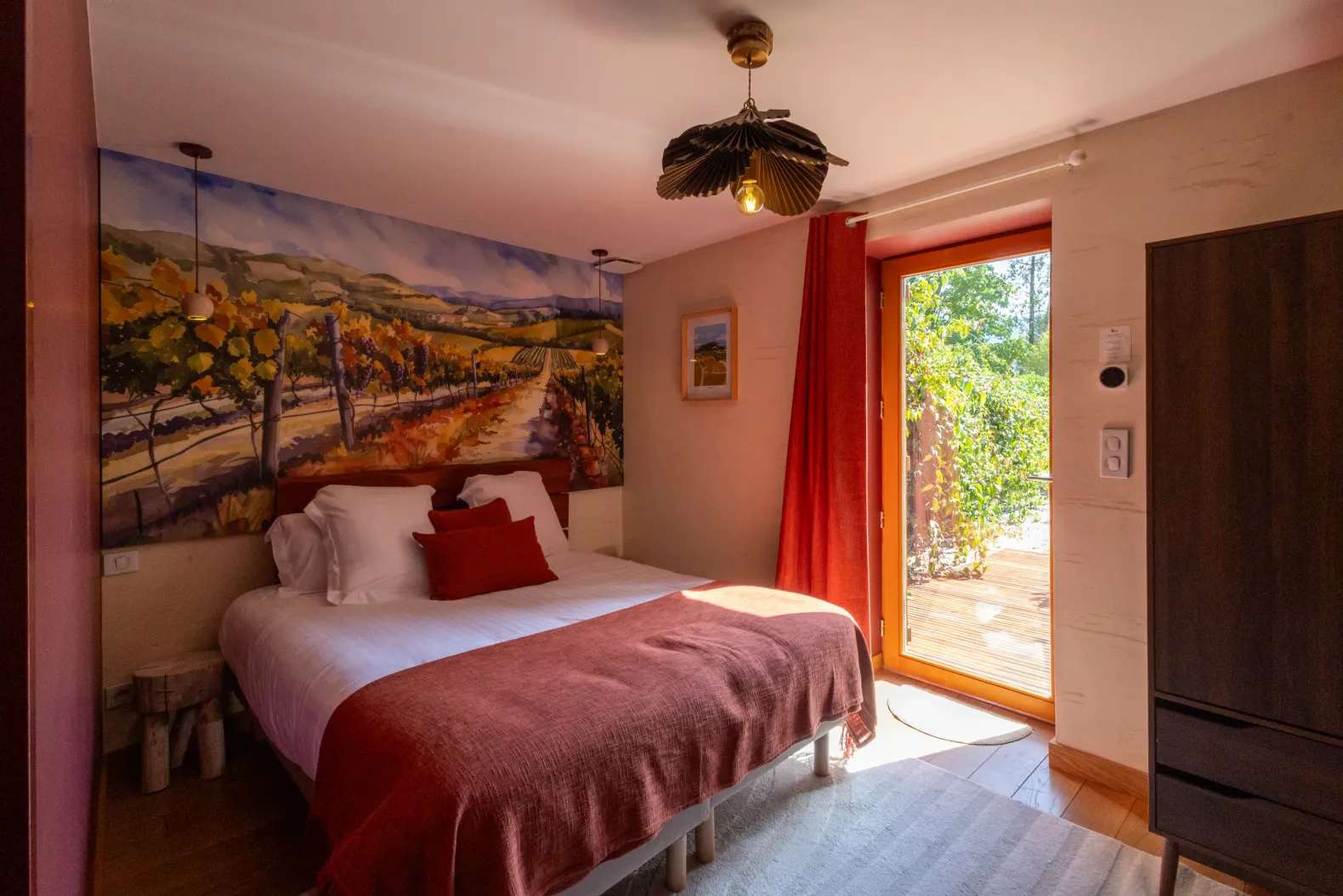 Chambre avec un lit double, une porte vitrée donnant sur une terrasse et une peinture murale représentant un vignoble
