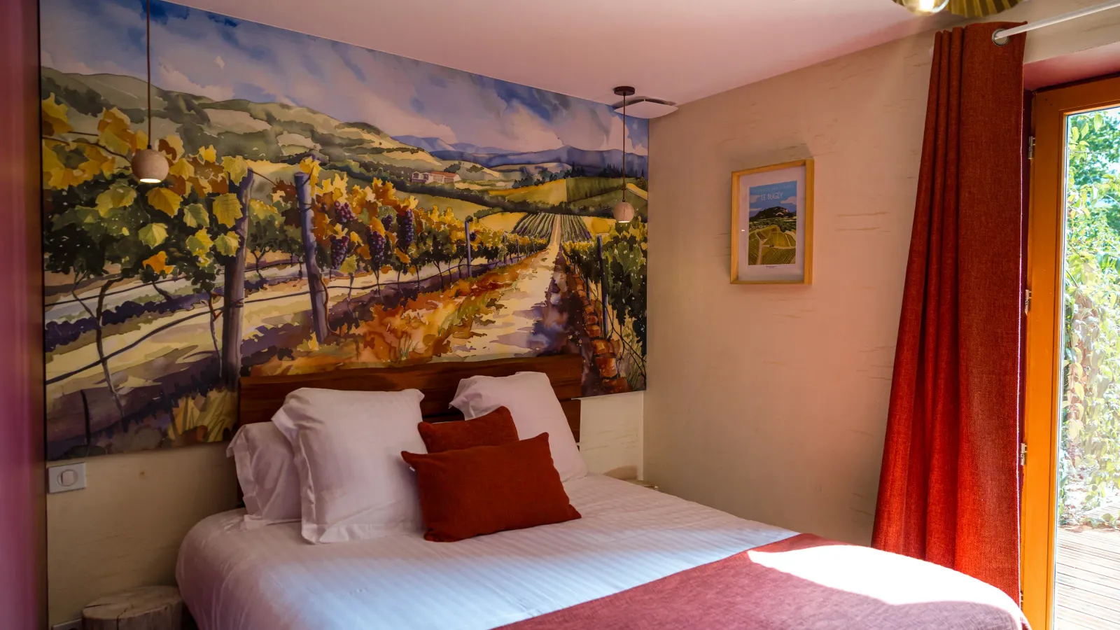 Chambre avec un lit recouvert d'une couverture beige et de coussins rouges, un mur peint représentant un vignoble et une porte vitrée donnant sur l'extérieur