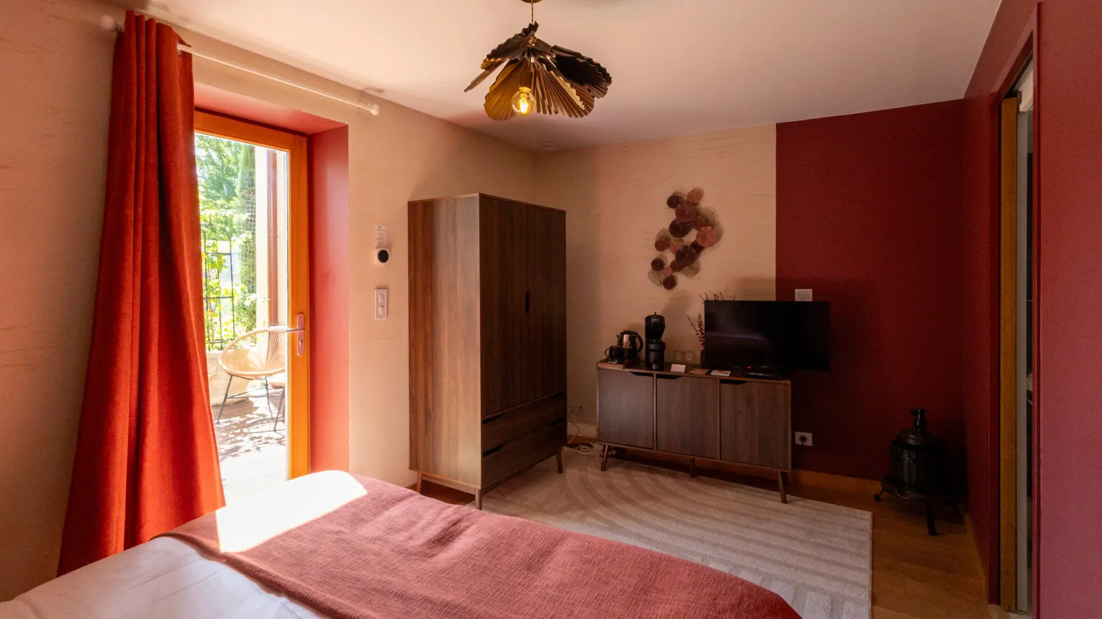Chambre avec lit, armoire, télévision, porte-fenêtre ouverte sur une terrasse et décoration murale