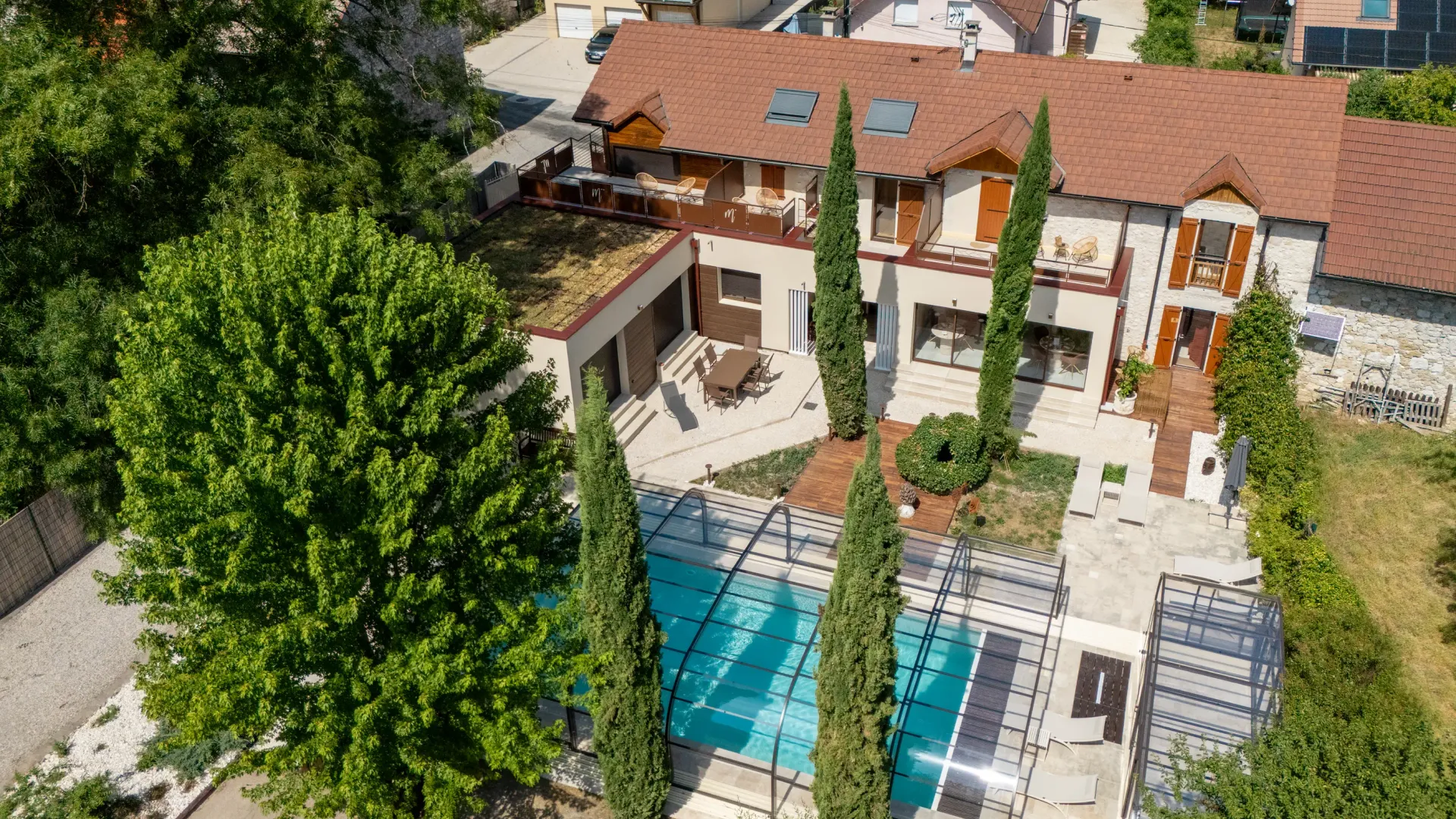 Maison avec piscine et terrasses entourée d'arbres et d'autres habitations